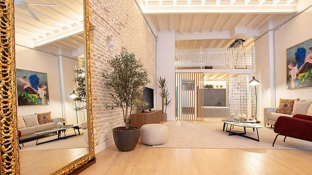 A modern living room with a large mirror, wooden flooring, a potted plant, a sofa, a red armchair, and a coffee table. - Genteel Home Santas Patronas V (Seville)