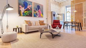 A modern living room with a sofa, coffee table, and red armchair. There are two paintings on the wall, a lamp, and a kitchen area in the background. - Genteel Home Santas Patronas V (Seville)