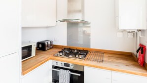 Une cuisine de taille réduite avec des meubles blancs, une cuisinière à gaz, un four à micro-ondes et un grille-pain.