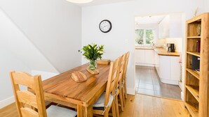 Un coin repas avec une table en bois, des chaises, un vase de fleurs et une horloge au mur.