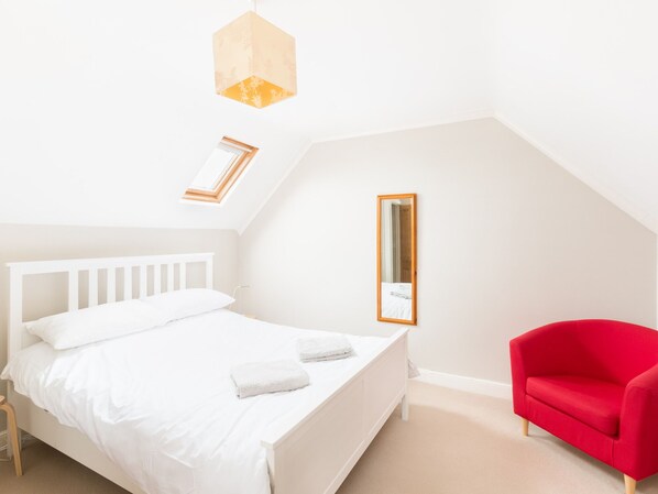 A bedroom with a white bed, a red chair, and a skylight.
