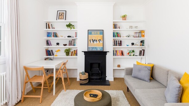 A living room with a fireplace, two bookshelves, a sofa, a coffee table, and a dining area with a table and chairs. - Cosy 1Bed Flat, Leamington Spa - Pass the Keys (Leamington Spa)