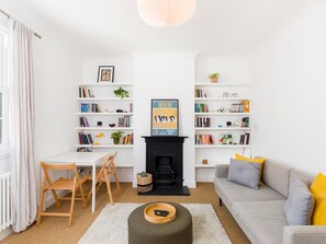 Ein Wohnzimmer mit Kamin, zwei Bücherregalen, einer Couch, einem Couchtisch und einem Essbereich mit Tisch und Stühlen.
