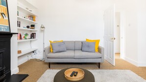 A living room with a grey sofa, yellow cushions, a wooden coffee table with remotes, a white bookshelf, and a white door. - Cosy 1Bed Flat, Leamington Spa - Pass the Keys (Leamington Spa)