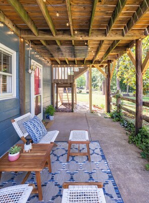 Een terras buiten met houten meubilair, een pergola en uitzicht op de achtertuin.