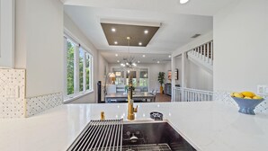 Una cucina moderna con isola centrale, zona pranzo con lampadario e scala che conduce a un altro livello.
