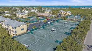 A residential area with multiple tennis courts surrounded by houses and a beach in the background.