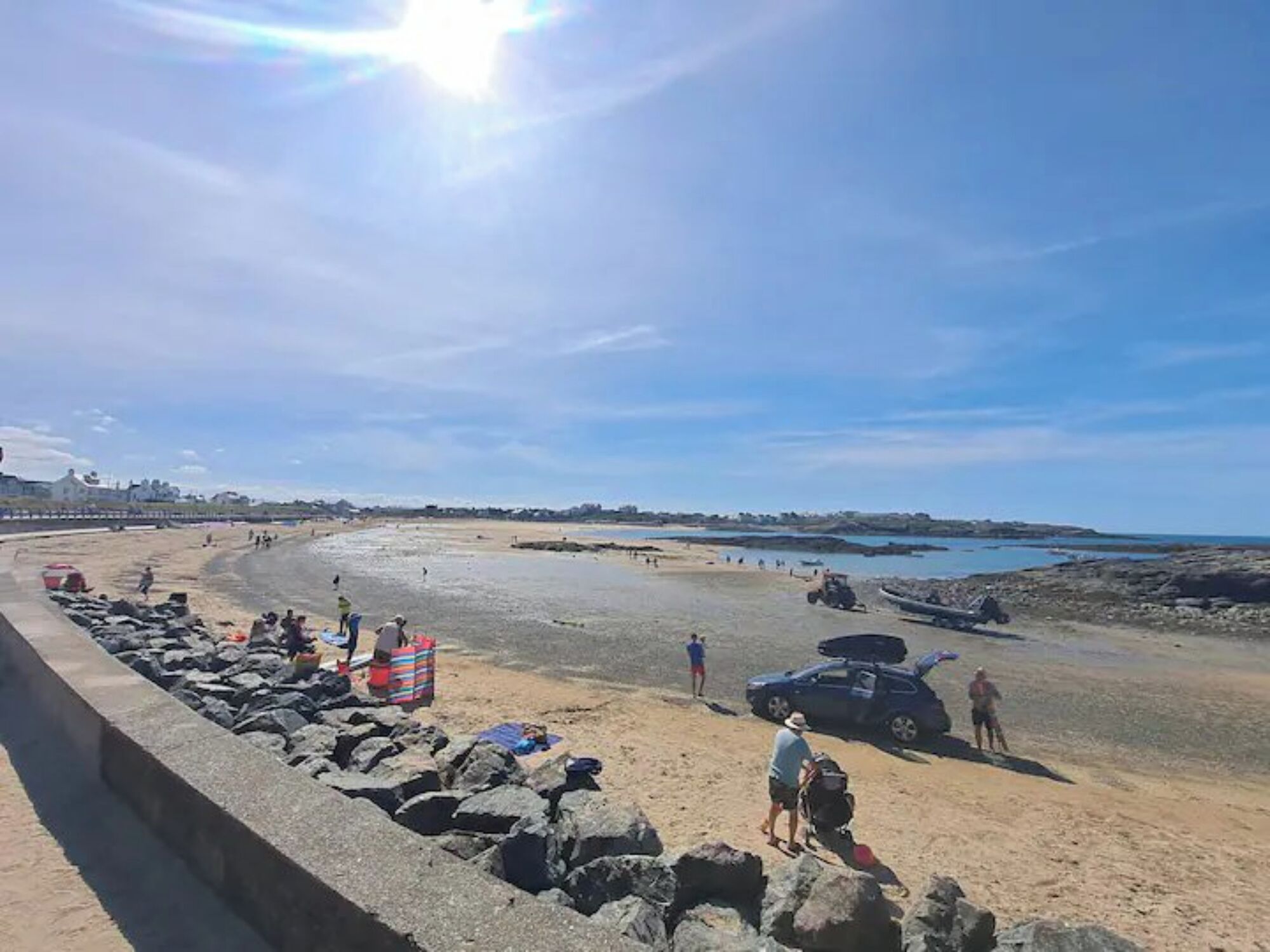 Ein Strand mit einer Betonbarriere, felsigem Gelände und einigen Personen.