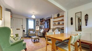 Ein gemütliches Wohnzimmer mit einem grünen Sessel, einem Holzesstisch und einem Bücherregal voller Bücher und Dekoration.
