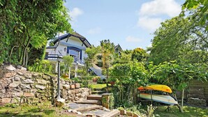 Un escalier en pierre mène à une maison à l’extérieur bleu et blanc, entourée d’une végétation luxuriante et d’un petit jardin.