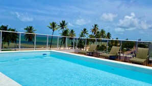 A clear blue pool with lounge chairs and a view of the beach and palm trees. - PUERTO VENTURA Flat by Penareia.tur.br (João Pessoa)
