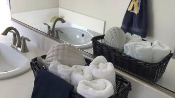 Ett badrum med ett vitt handfat, en spegel och två korgar av rotting som innehåller handdukar och en dekorativ detalj.