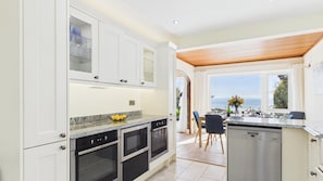 A modern kitchen with white cabinets, a granite countertop, and a view of the sea.