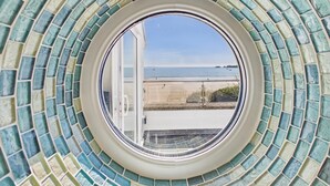 A circular window with a view of a beach and sea. - Rainbow Leap - 5 Bed Holiday Home - Saundersfoot (Saundersfoot)