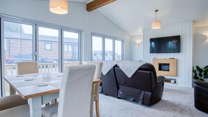 Een moderne woonkamer met een bank, een televisie en een open haard. Er zijn grote ramen en een balkon te zien.