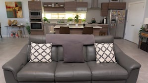 Un soggiorno moderno con un divano in pelle grigio, due cuscini decorativi a motivi e un tavolino da caffè, oltre a un tappeto decorativo.