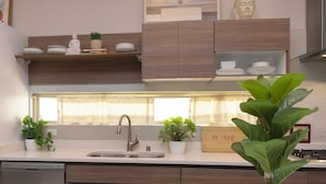 Una cucina moderna con un piano di lavoro bianco, lavello in acciaio inossidabile e mobili in legno. Sul piano di lavoro ci sono piante in vaso e una statua di Buddha sullo scaffale.