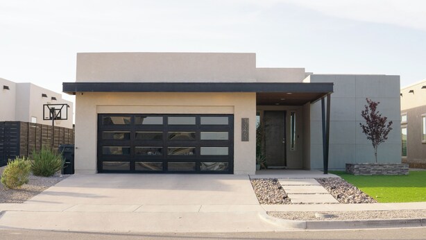 Una casa moderna a due piani con garage, un piccolo giardino antistante con un albero e un canestro da basket.