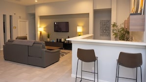 Un soggiorno moderno con un divano, una TV, un angolo bar con sgabelli e una ventola a soffitto.