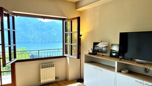A room with a large window offering a view of a lake and mountains, a white cabinet, and a flat-screen TV. - Magic View - Love Escape for Two (Tremezzo)