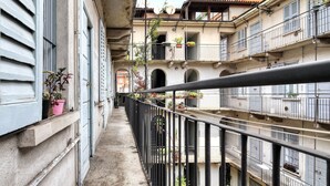 Un carrer urbà estret amb balcons, plantes en testos i un cel serè.