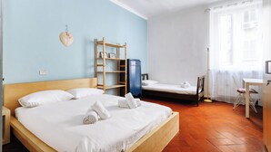 Una habitació amb dos llits, escriptori, cadira, armari i una estant amb objectes.