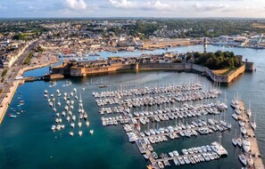 Une vue aérienne d’une marina où sont amarrés de nombreux bateaux, entourée d’un port fortifié et avec une vue sur la ville en arrière-plan.