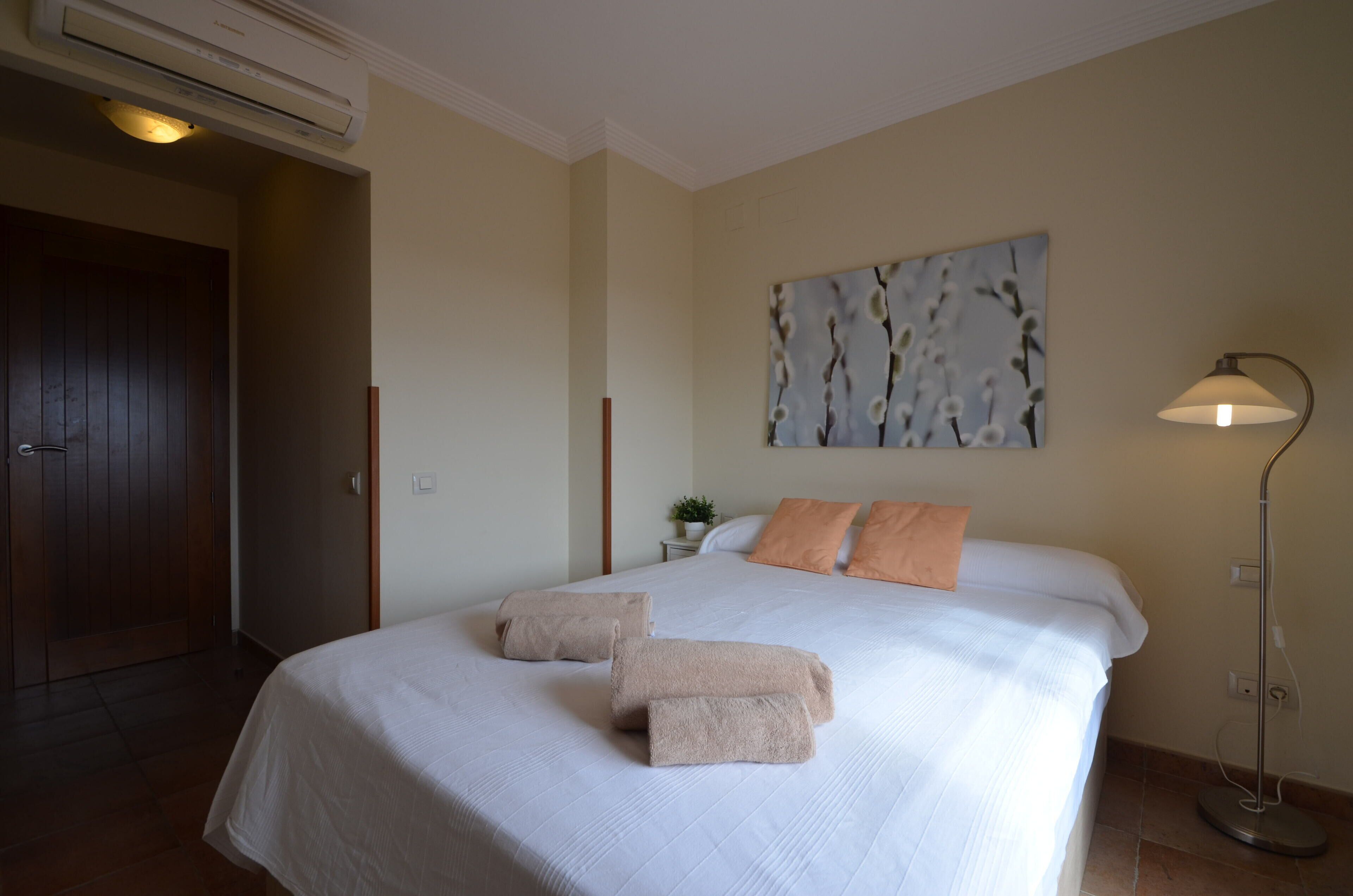 A hotel room with a large bed, two pillows, a bedside lamp, and a painting on the wall.