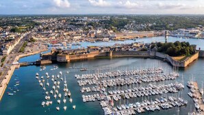 Un port amb nombroses embarcacions amarrades, una fortificació i un paisatge urbà al fons.