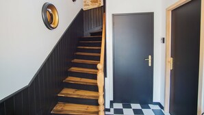 Una escala de fusta amb barana negra que condueix a una porta fosca amb mànec daurat.