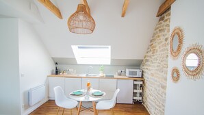A modern kitchen with a dining table, white chairs, a hanging light fixture, a stone wall, and a small window. - -PICCO BIANCO-STUDIO ENTIÈREMENT RÉNOVÉ-CONCARNEAU (Concarneau)