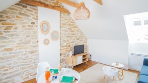 A cozy room with a stone wall, wooden beams, a TV, a dining table, and a blue chair. - -PICCO BIANCO-STUDIO ENTIÈREMENT RÉNOVÉ-CONCARNEAU (Concarneau)