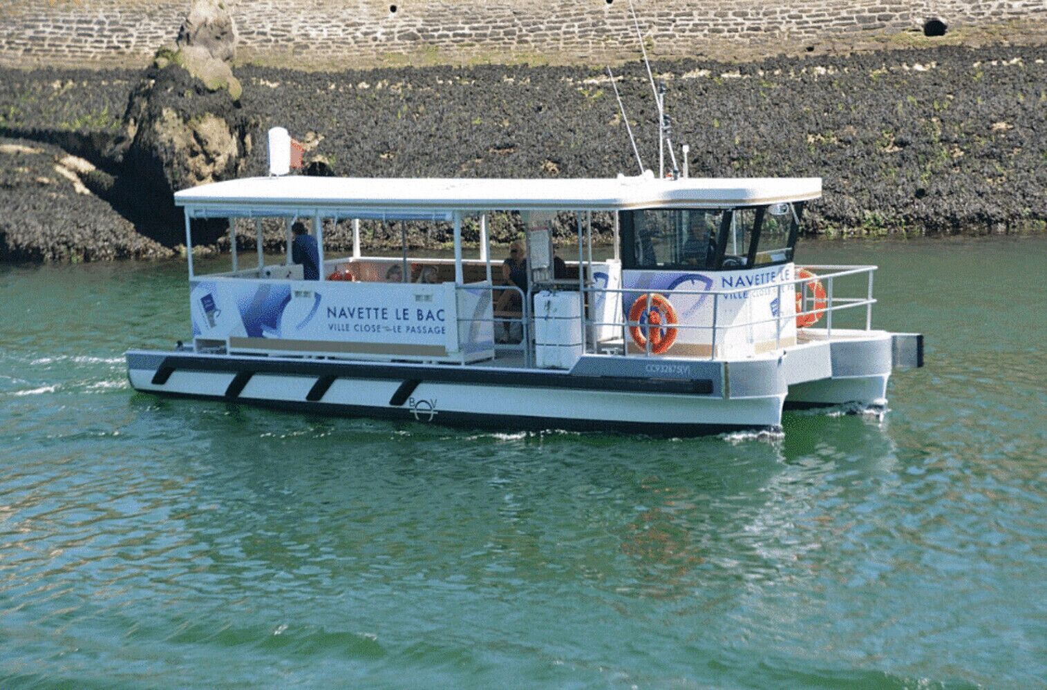 A boat with a covered deck, a lifebuoy, and a sign reading 'NAVETTE LE BAC.'