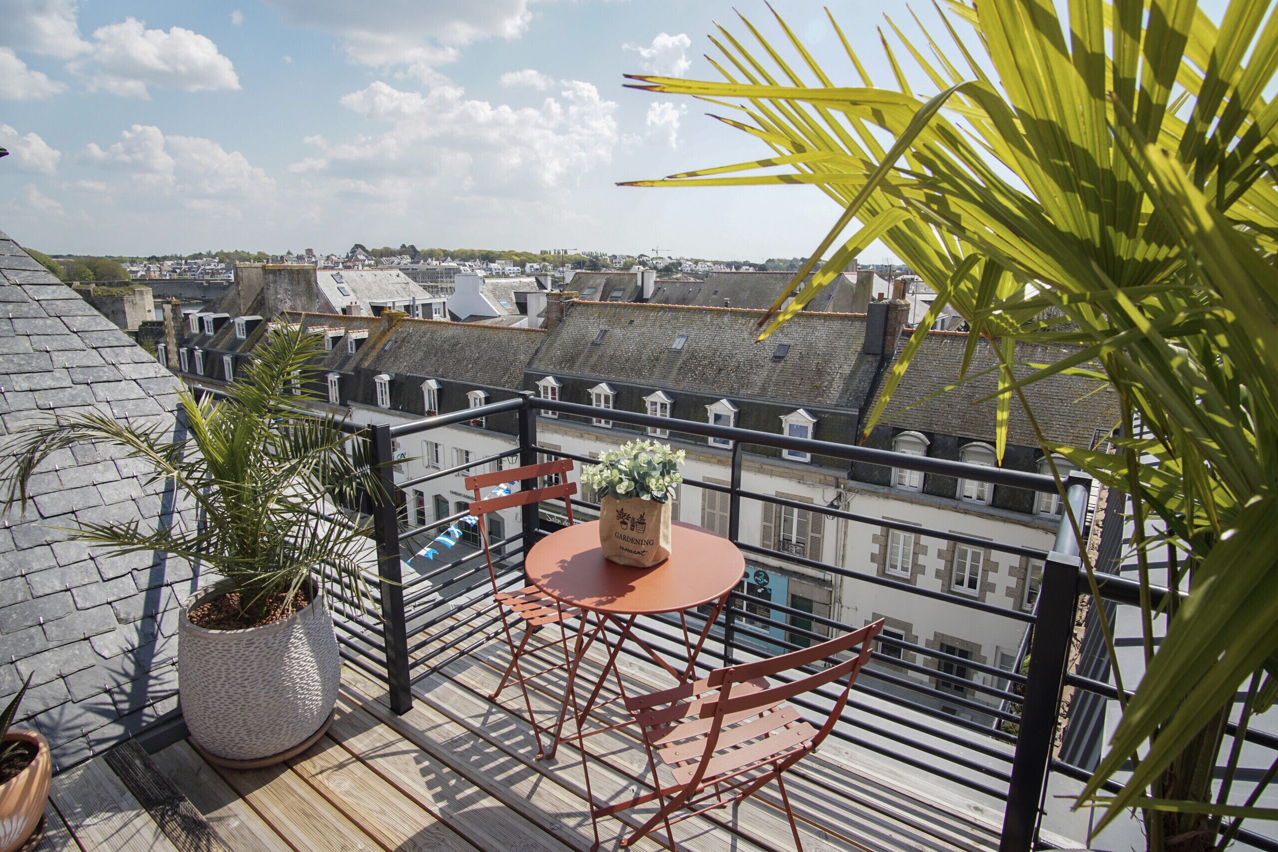 Een balkon met een ronde tafel en stoelen, een bloempot en uitzicht op de stad.
