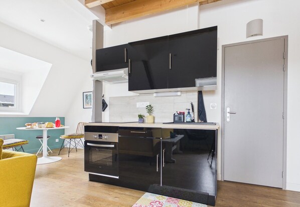 Uma cozinha compacta com armários pretos, forno embutido e um espaço de refeições com mesa e cadeiras.