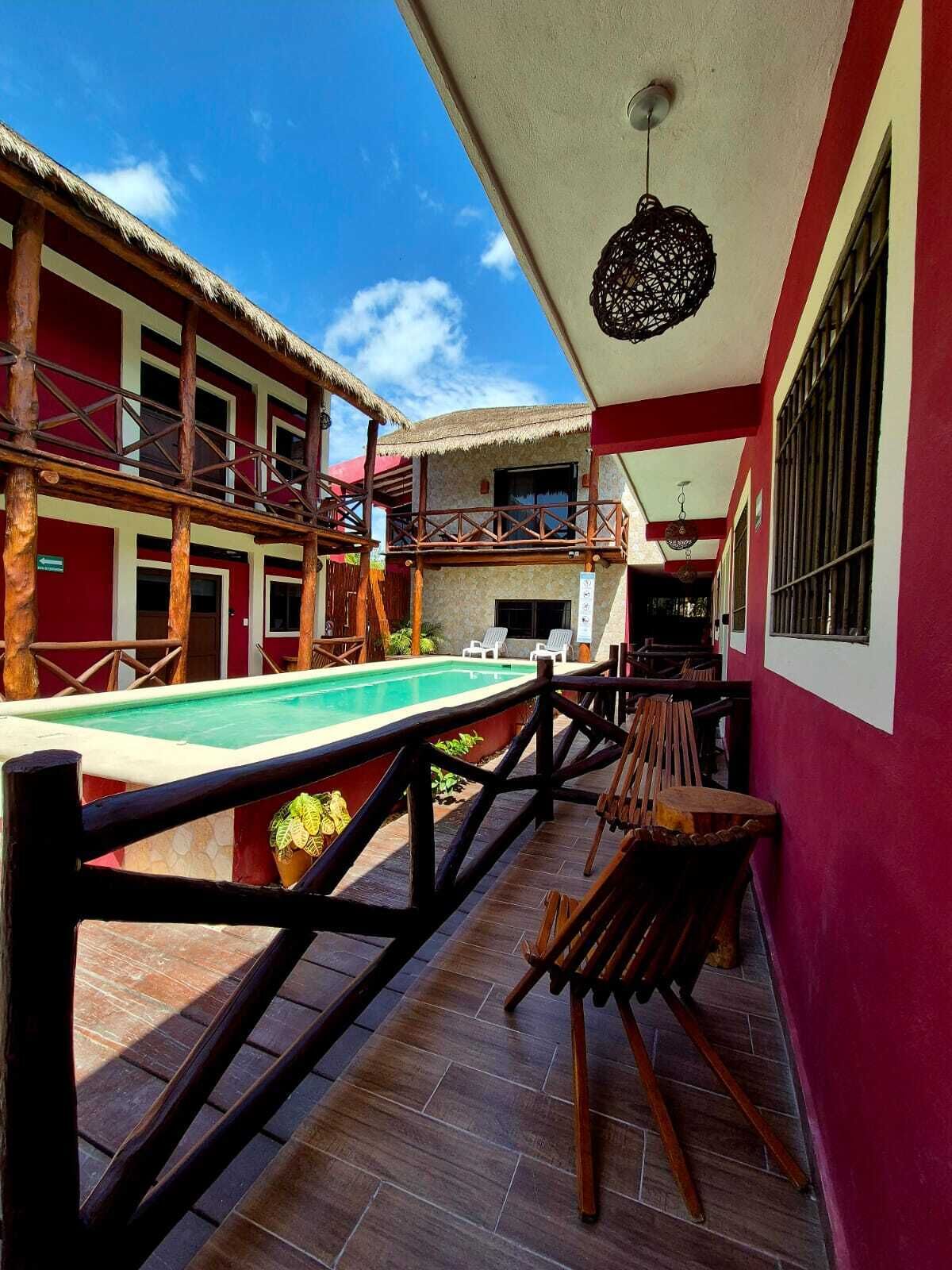A pool area with a wooden deck, lounge chairs, and a thatched-roof building.