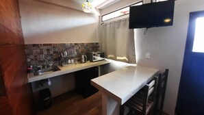 Eine kompakte Küche mit gefliestem Spritzschutz, einer kleinen Arbeitsfläche, einem Spülbecken, einem Toaster und einem an der Wand befestigten Fernseher.