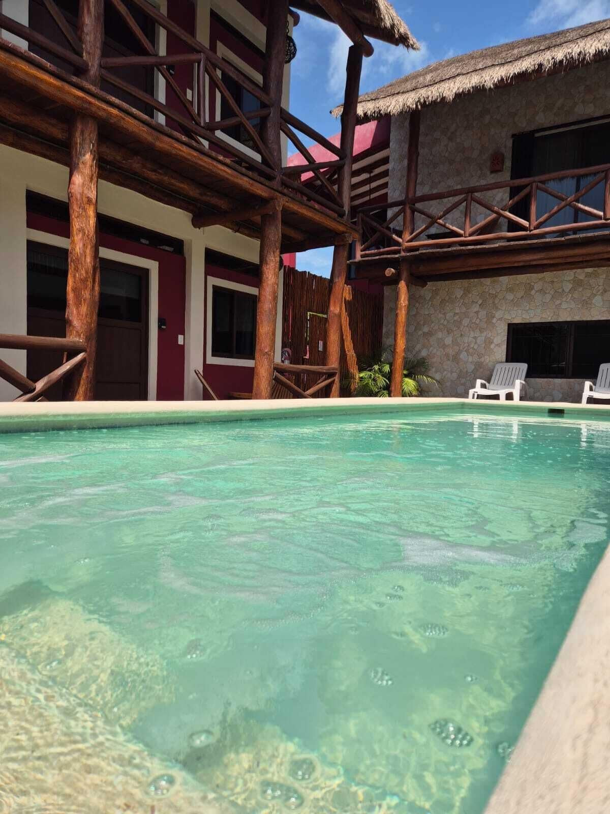 A pool area with clear water, wooden deck, and white lounge chairs.