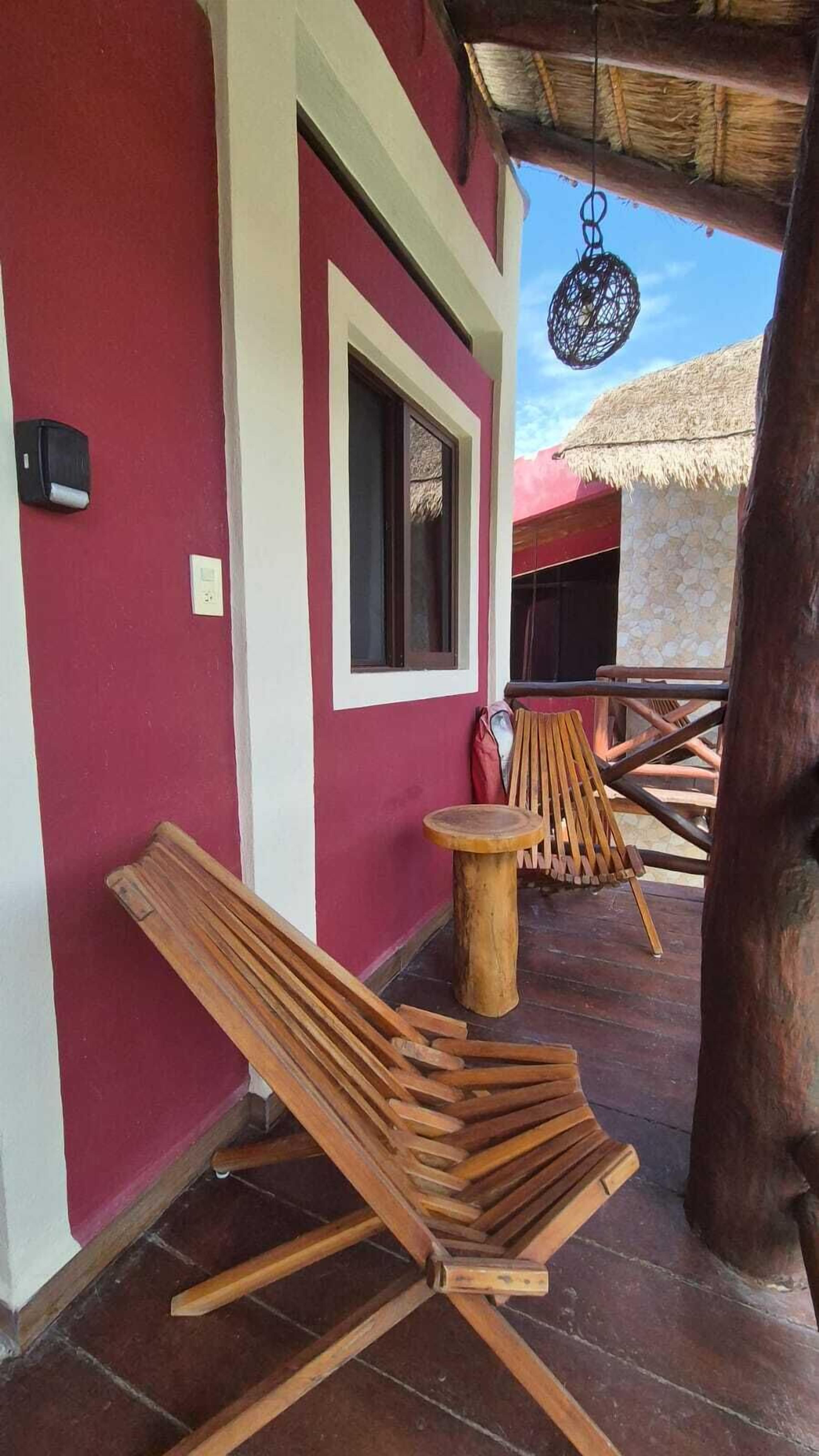 A covered outdoor seating area with wooden loungers and a thatched roof structure in the background.