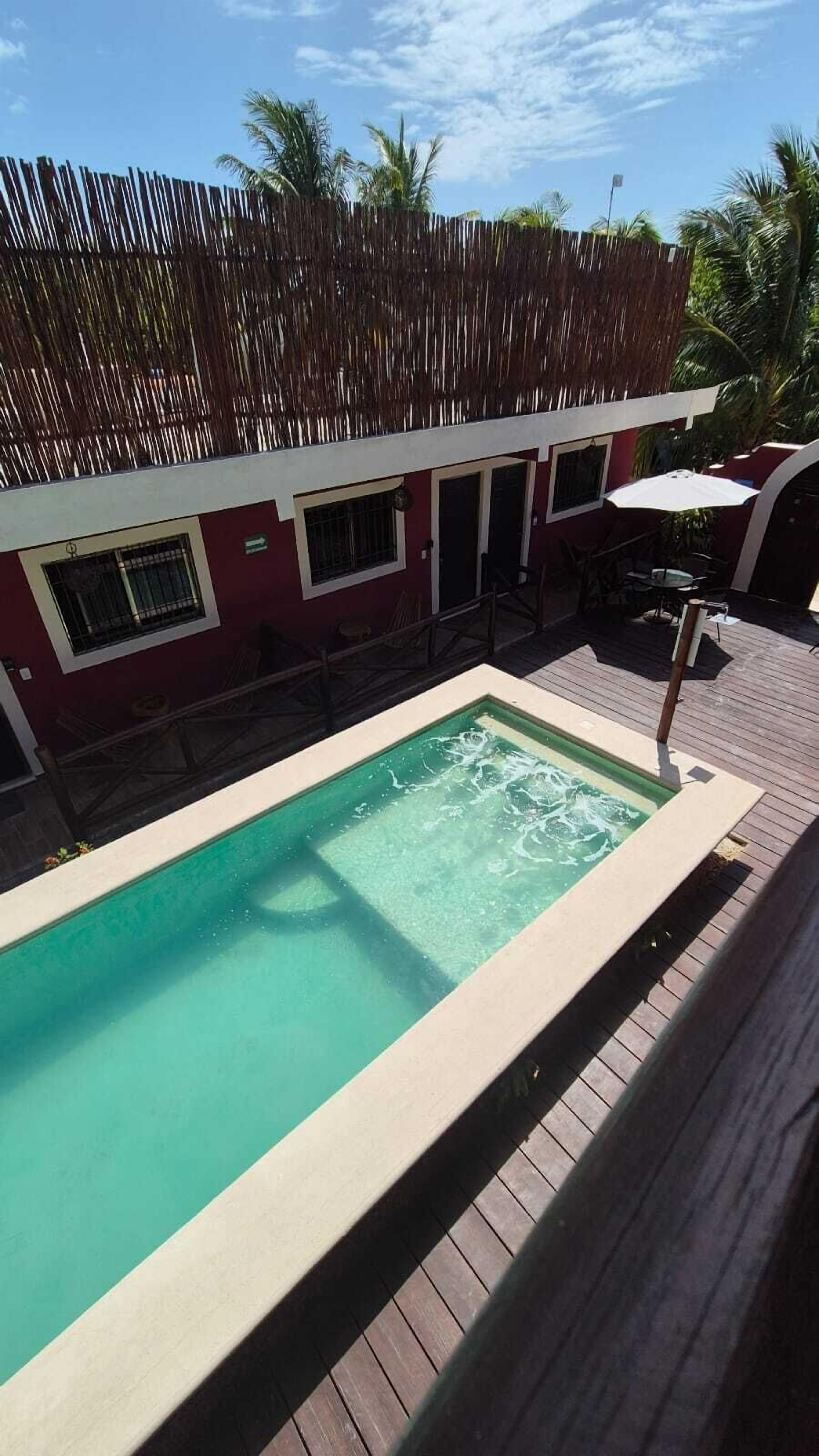 A rectangular pool with clear water, surrounded by a wooden deck and a red building with windows and a door.