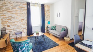 A room with a stone wall, a grey sofa, a small round table, a blue armchair, and a wooden desk with a computer.