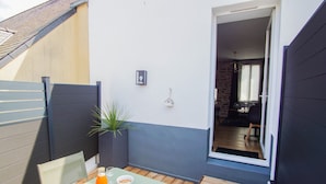A small patio with a table, chairs, a potted plant, and a bottle of orange juice.