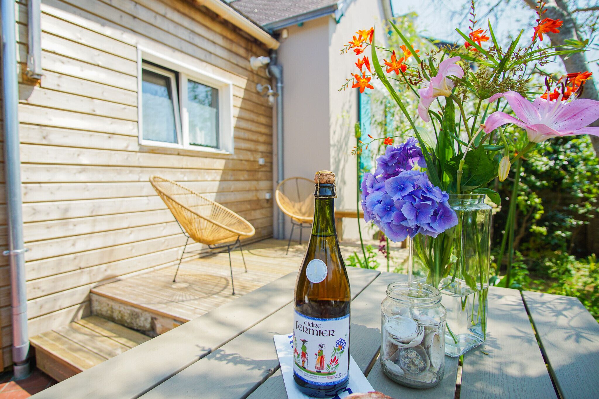 A bottle of Cider Germier on a table with a wicker chair and a vase of flowers.