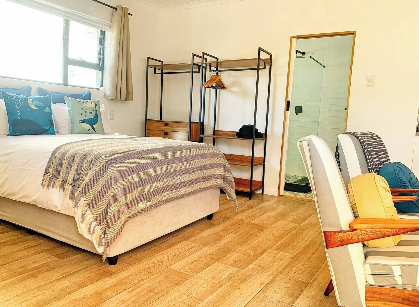 A bedroom with a bed, a wooden floor, a chair, a shelf unit, and a door.