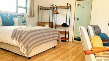 A bedroom with a bed, a wooden floor, a chair, a shelf unit, and a door.