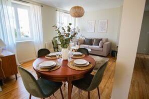 Un coin repas avec une table ronde dressée pour quatre personnes, entourée de chaises, un vase avec des fleurs et un luminaire suspendu.