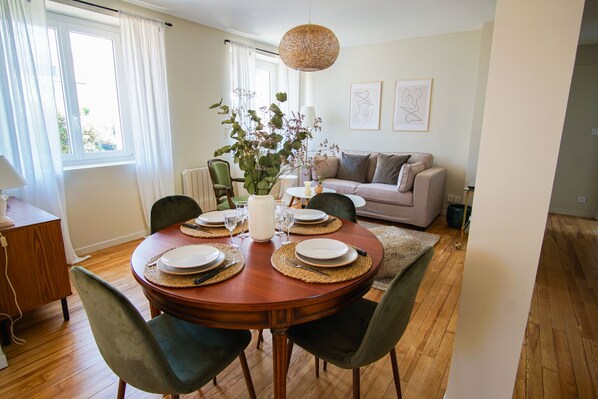 Een eetgedeelte met een ronde tafel voor vier personen, omringd door stoelen, een vaas met bloemen en een hanglamp.