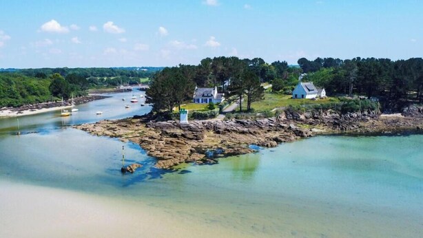 A coastal landscape with a sandy beach, a rocky shoreline, and a few houses near the water. - -BOSCO- ÉLÉGANT T3 AVEC BALCON ET VUE SUR LE PORT (Concarneau)