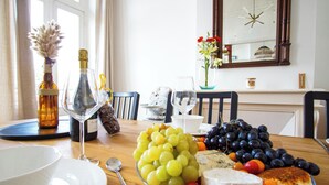A dining table with a bottle of wine, a glass, a bowl, a plate, a spoon, a bunch of grapes, a bunch of blueberries, and a piece of cheese. - -BOSCO- ÉLÉGANT T3 AVEC BALCON ET VUE SUR LE PORT (Concarneau)