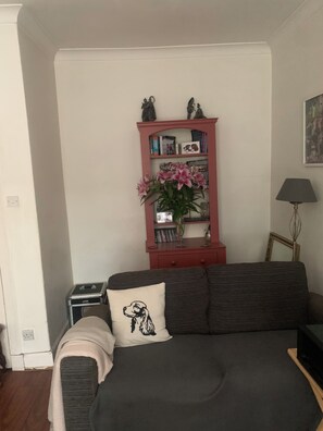 A living room with a dark sofa, a small side table, a red bookshelf, and a framed picture on the wall. - Edinburgh City Escape - Large 1 Bedroom Apartment (Edinburgh)